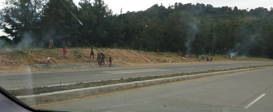 Alongside the highway, children stay warm near fires as they wave at passing cars hoping for a Christmas gift.